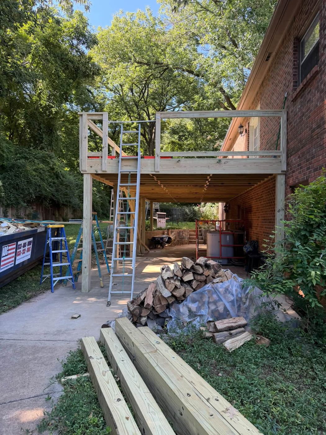 Elevated deck framing in progress against a brick house with posts and joists in place