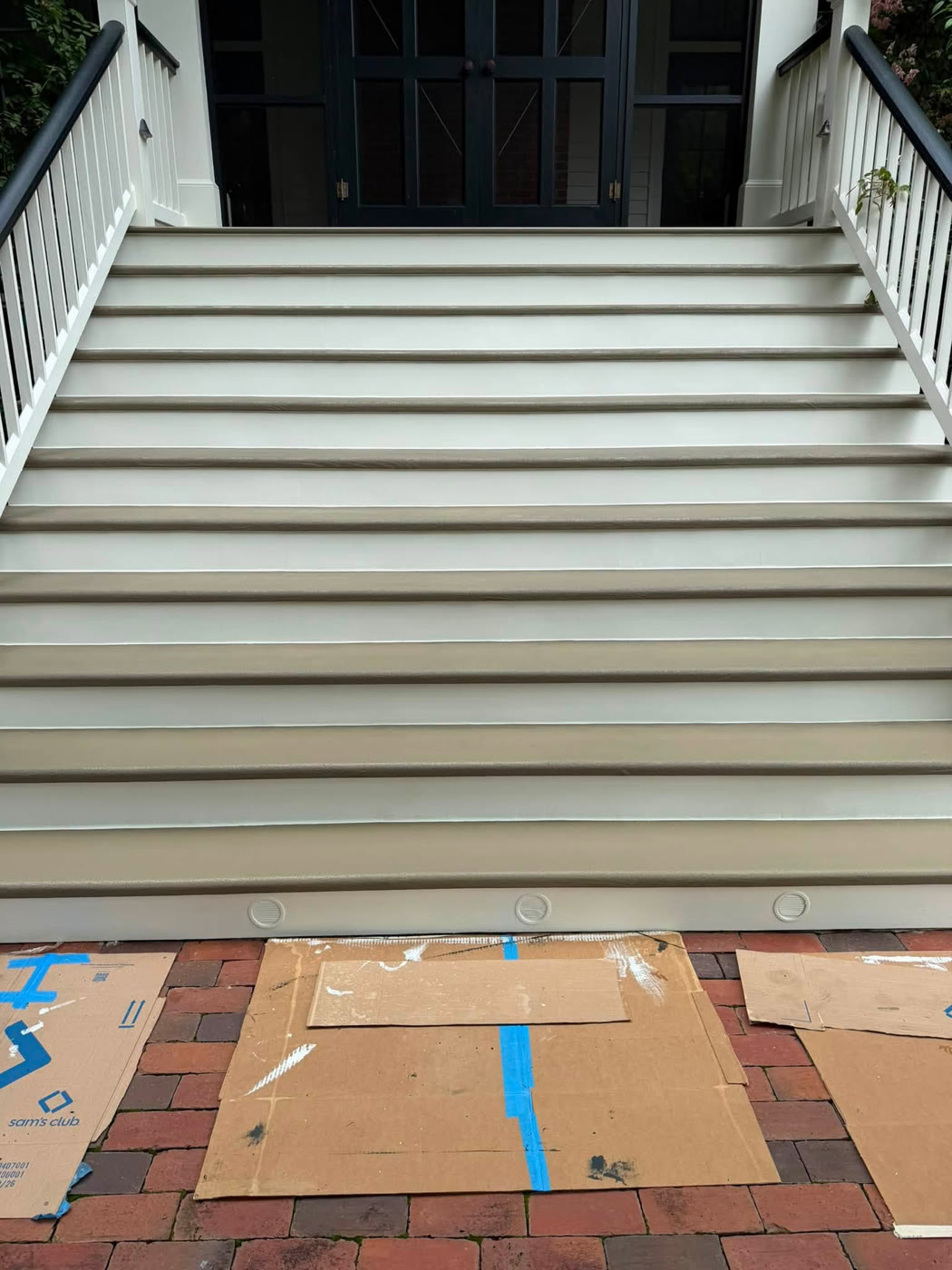 Finished entrance stairs with tan treads, white risers, and white railings leading to double doors